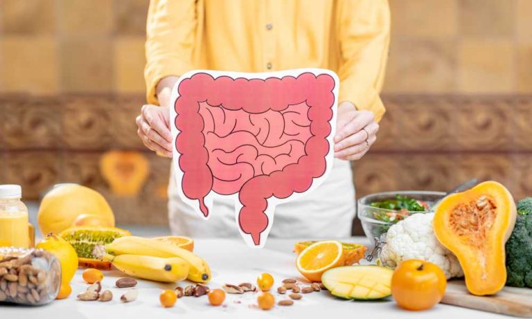 person in yellow shirt holding picture of the colon behind a table of colorful fruit and vegetables