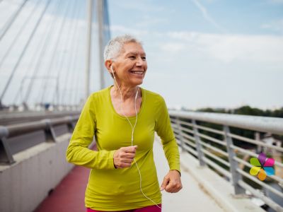 smiling older woman with short greay hair running along a bridge in sunshine