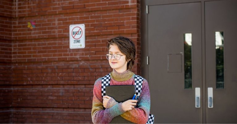 young person with rainbow jumper holding book at school entry.
