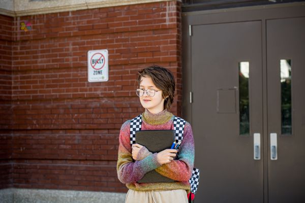 teenage stands at school door clutching folder.