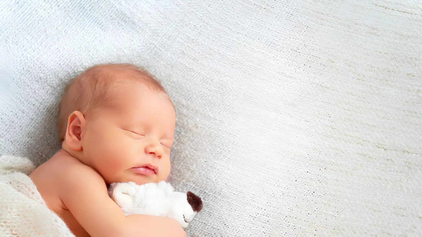 baby sleeping and cuddling a white teddy