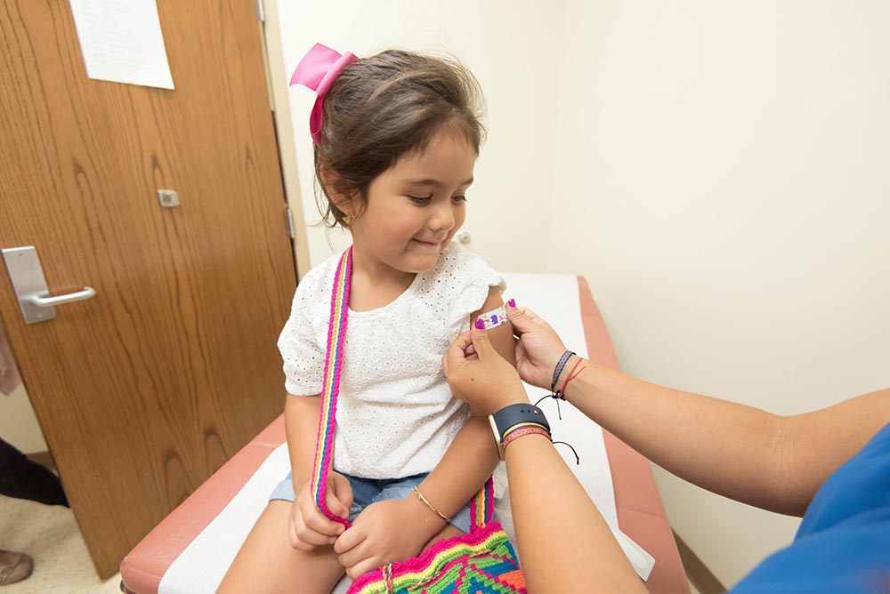 little girl smiles looking at colourful bandaid on shoulder