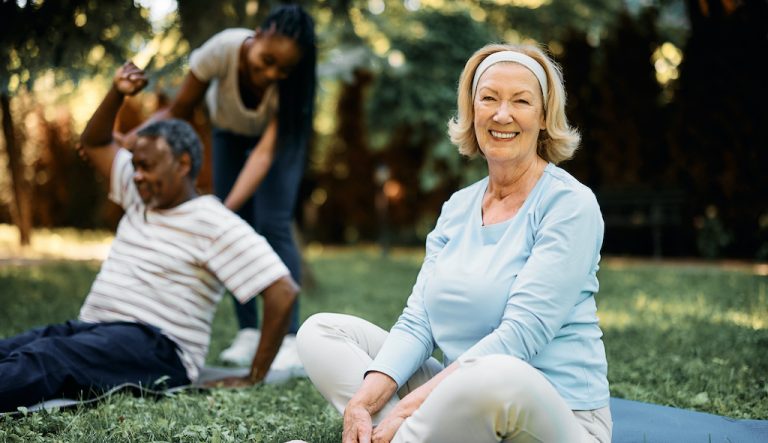 woman sitting in a park doing group exercises and smiling at the camera