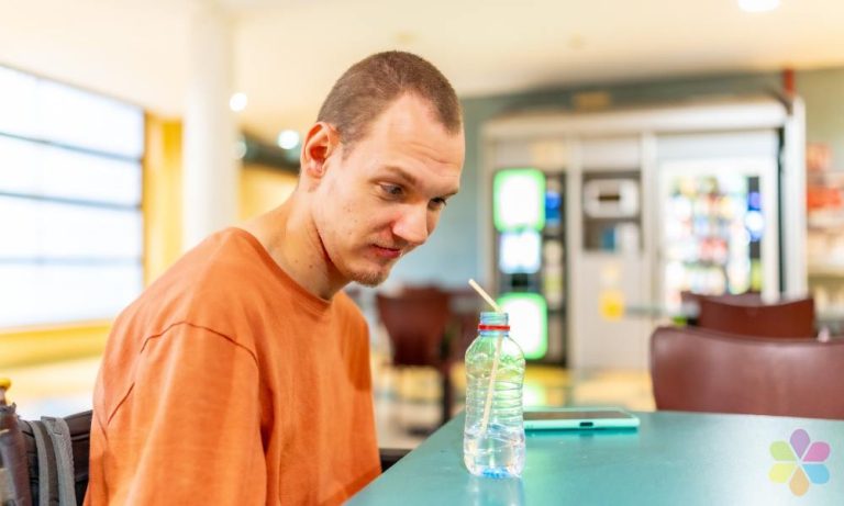 an in orange tshirt looks quizzically at a drink with a straw.