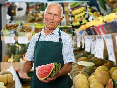 older man in green grover holding an open watermelon and smiling